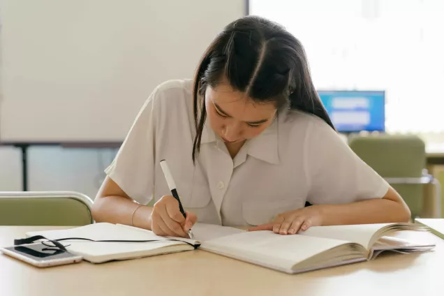 Kvinna med långt hår sitter och skriver i en skrivbok. foto